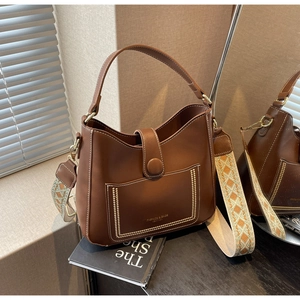 Brown leather bucket bag with a colorful ethnic woven shoulder strap on a book