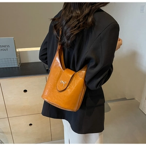 Detail of orange-brown bucket bag with silver bow hardware worn as a shoulder bag