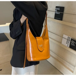 Detail of a ginger yellow bucket bag with a silver bow clasp and thin leather shoulder strap