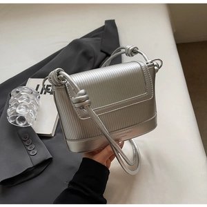 Detail of silver textured leather bag featuring knot strap and embossed logo design