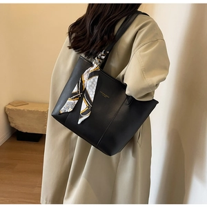Detail of black leather tote bag with silk scarf accent worn by model in trench coat