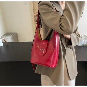Close-up of a red glossy leather shoulder bag featuring a silver metal bow detail