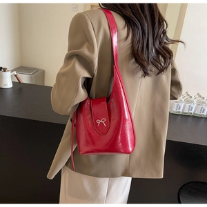 Detail of red glossy shoulder bag with silver bow ornament worn with casual office attire