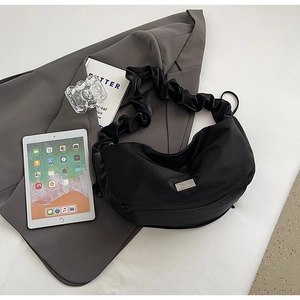 Détail du sac plissé noir avec logo argenté à côté d'une tablette et d'un blazer