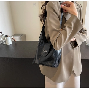 Detail of glossy black oil wax leather crossbody bag with silver bow accent