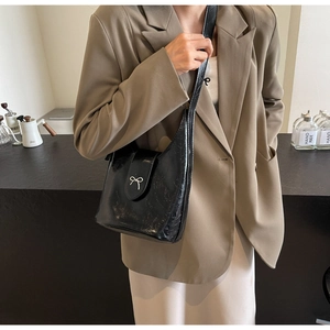 Detail of black cracked leather bucket bag with silver bow buckle on model outfit