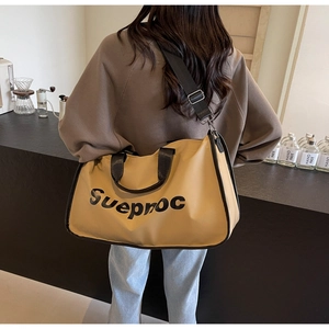 Detail of khaki travel tote with Sueproc logo, black trim, and adjustable shoulder strap