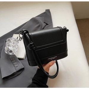 Detail of black textured crossbody bag with silver hardware and knotted shoulder strap