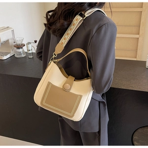Detail view of beige leather bucket bag with brown pocket and ethnic woven strap