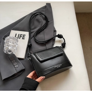 Detail of black leather square bag featuring pleated flap and unique knotted shoulder strap