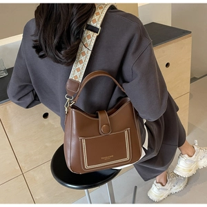 Detail of dark brown leather bucket bag with white stitching and ethnic jacquard strap