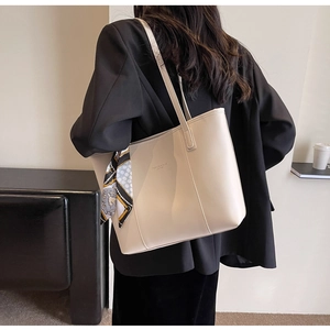 Detail of off-white leather tote bag featuring a decorative printed silk scarf on the handle