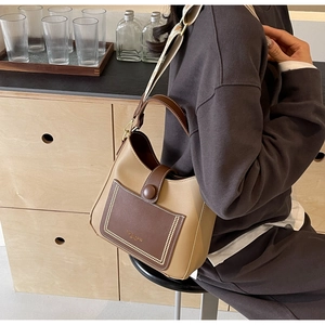 Detail of minimalist leather bucket bag with contrast pocket and embroidered strap