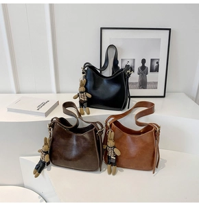 Three minimalist bucket bags in black and brown featuring rabbit charms in a studio setting
