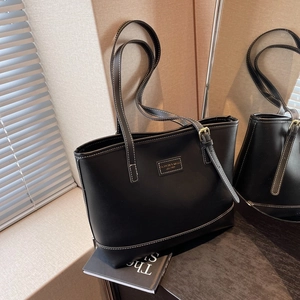 Close-up of black tote bag featuring white contrast stitching and metallic buckle details