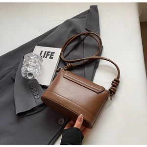 Detail of a brown leather crossbody bag with knotted strap on a grey suit and book