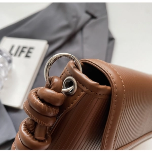 Detail of brown textured leather bag with silver ring hardware and knotted strap design