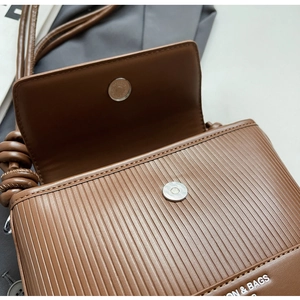 Detail of brown pleated faux leather texture with silver magnetic snap on a crossbody bag
