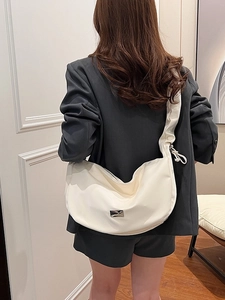 Grand sac demi-lune crème avec bandoulière plissée porté sur une veste de tailleur