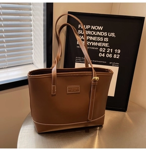 Detailed view of brown leather tote bag with white contrast stitching and logo plate