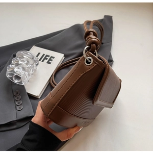 Close-up of brown crossbody bag with vertical striped embossing and knotted strap detail