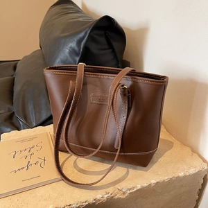 Detail of a brown tote bag with contrast stitching and branded leather patch on a stone base