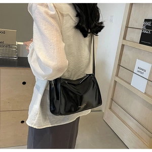 Gros plan d'un sac à bandoulière noir brillant avec logo porté par un mannequin chic