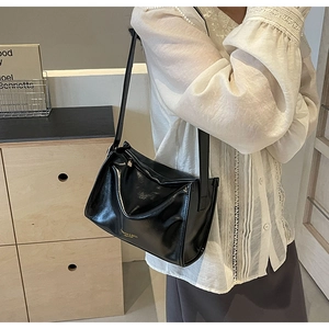 Détail d'un sac à bandoulière en cuir noir brillant avec texte doré sur un modèle