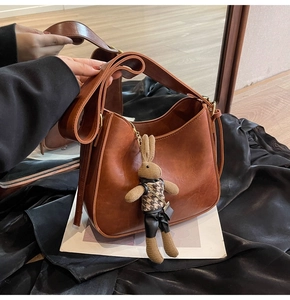 Detail of a brown leather bucket bag featuring a wide strap and a cute rabbit plush charm