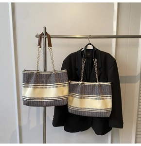 Detail of woven straw tote bag featuring golden chain straps and striped patterns