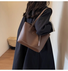 Brown leather tote bag featuring contrast stitching and large capacity on a model's shoulder