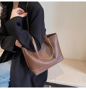 Close-up of a large dark brown leather tote bag with contrast stitching worn on a shoulder