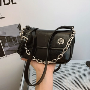 Detail view of a black glossy leather handbag with silver chain and metal logo