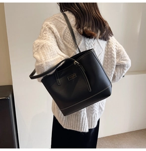 Detail showing the white contrast stitching and logo plate on a black leather tote bag