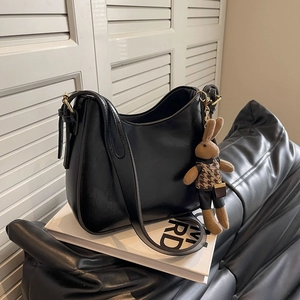 Macro detail of black leather bucket bag featuring a cute knitted rabbit charm accessory
