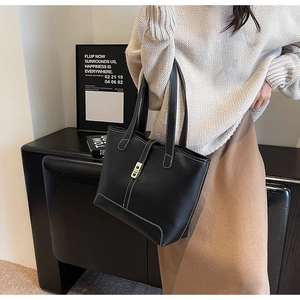 Detail of black leather tote bag with white stitching and gold buckle on a sweater model