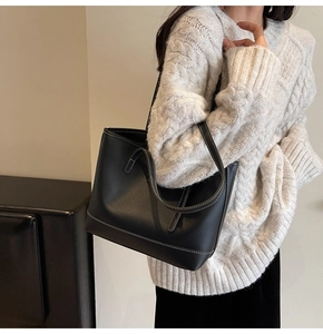 Close-up of black leather tote bag featuring white contrast stitching and long handles