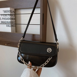 Detail of glossy black leather crossbody bag with silver chain and metal logo accent