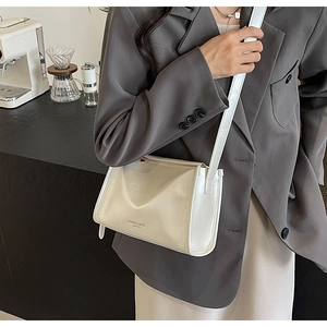 Détail du sac bandoulière blanc en cuir avec logo porté par un mannequin dans un café