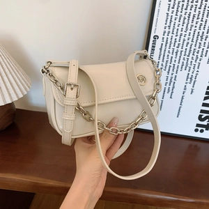 Detail of a creamy white leather shoulder bag with gold chain and circular metal logo
