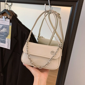 Detail of a beige leather flap bag with silver chain strap and metal logo on a hanger