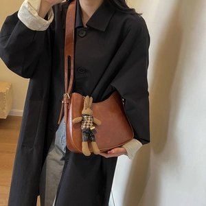Close-up of retro brown hobo bag featuring a cute knitted bunny doll pendant on strap