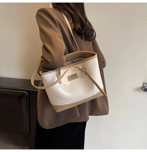 Detail of a beige and khaki contrast tote bag worn over the shoulder with a blazer