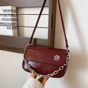 Close-up of wine red glossy pleated crossbody bag with silver chain and metal logo detail