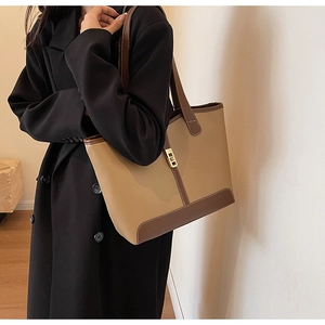 Close-up of a two-tone tote bag with a golden metal lock worn by a model in a warm setting