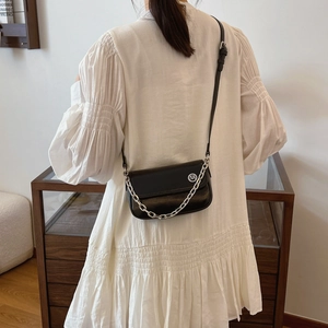 Detail of a chic black crossbody bag with silver chain worn over a white pleated dress