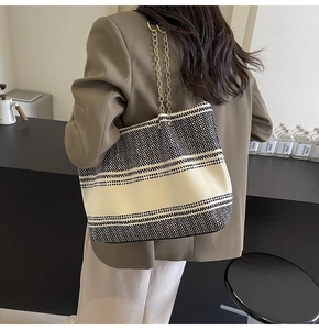 Detail of a large woven tote bag with black and white patterns and gold chain straps