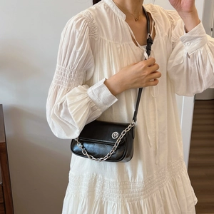 Detail of a black crossbody bag with silver chain strap and logo on a white dress
