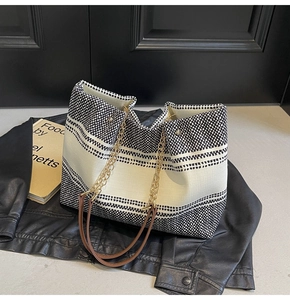 Detail of black and white striped tote bag with gold chain strap on black leather jacket