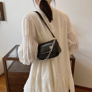 Close-up of stylish black glossy leather crossbody bag with bold silver chain detail